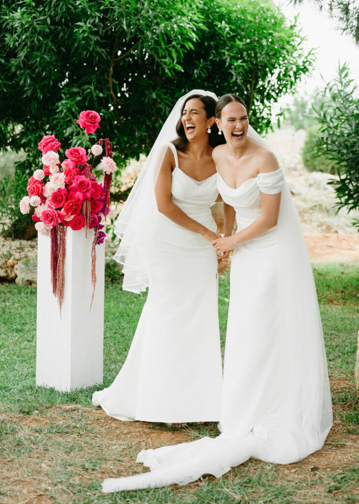 Wunderschöne lachende Bräute vor einem Blumengesteck auf ihrer Hochzeit.