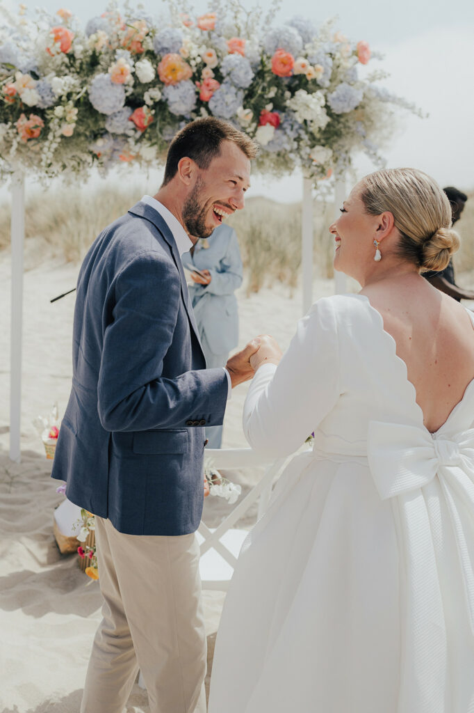 Hochzeitspaar am Strand vor einem Blumen Traubogen.